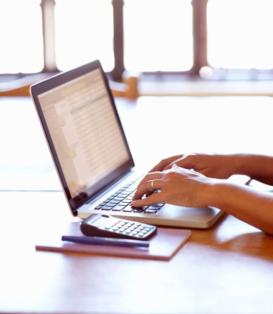 Calculating her tax for the month. Closeup detail view of female hands using a laptop.